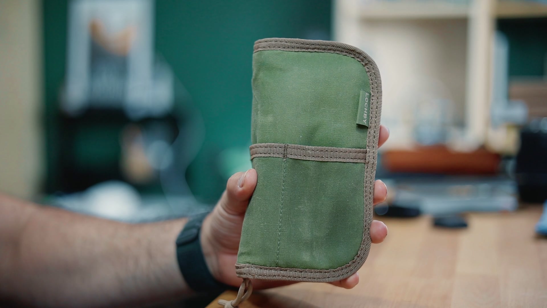 Closed Lochby Quattro pen case in olive waxed canvas with a front strap, held in hand.
