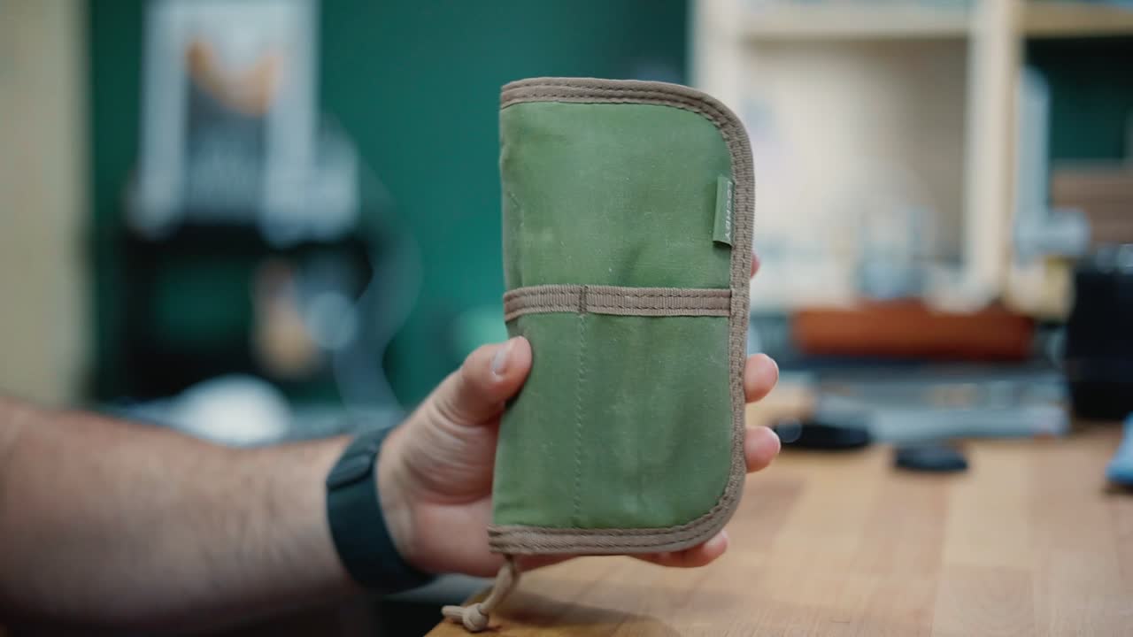 LOCHBY Quattro closed, olive waxed canvas, front strap, held in hand.