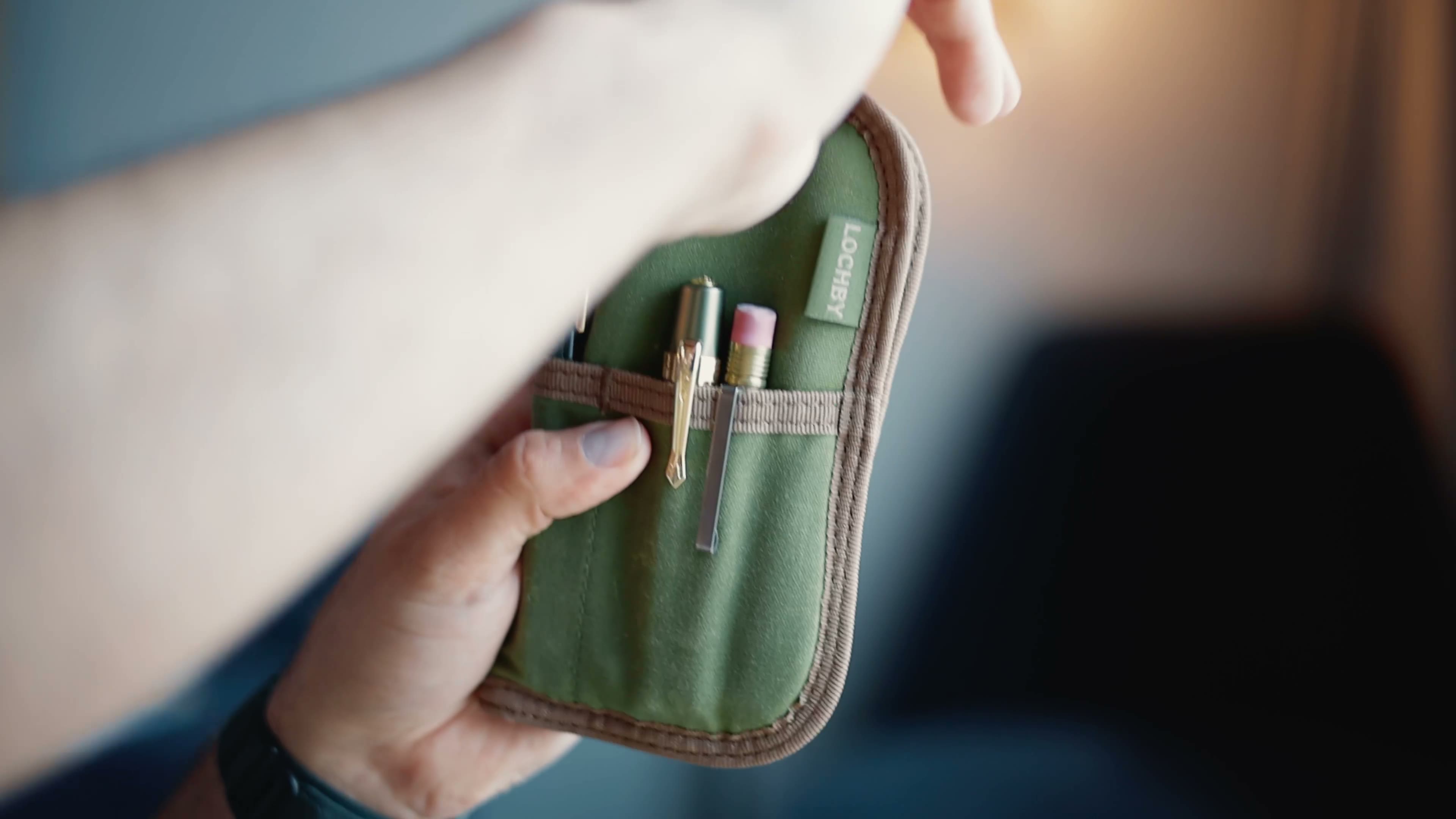 LOCHBY Quattro. Olive fabric pen case open in hands; LOCHBY tab; pens in elastic slots.