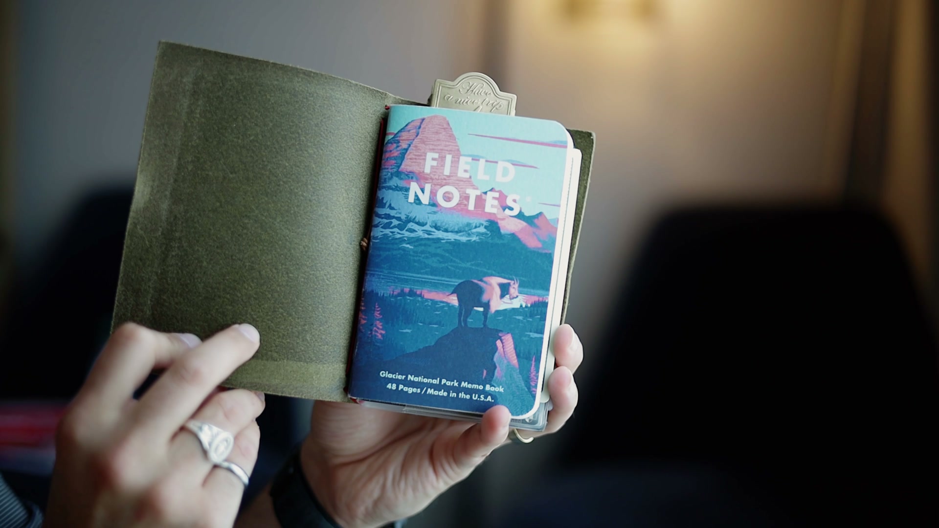 Dark olive-green leather Paper Republic notebook cover held in hand, with a brass bookmark clip and an LFD monogram